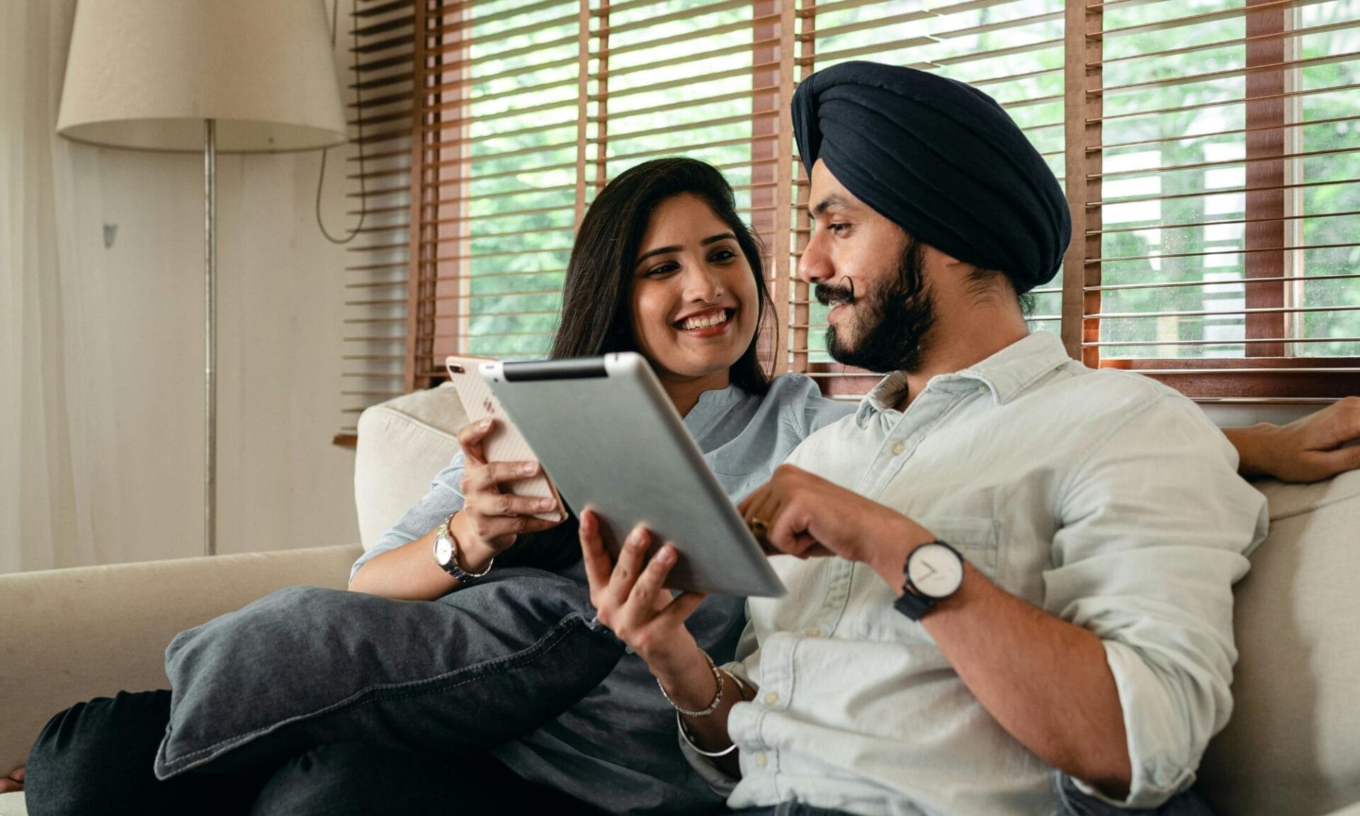 Couple sat on sofa, looking at a phone and tablet