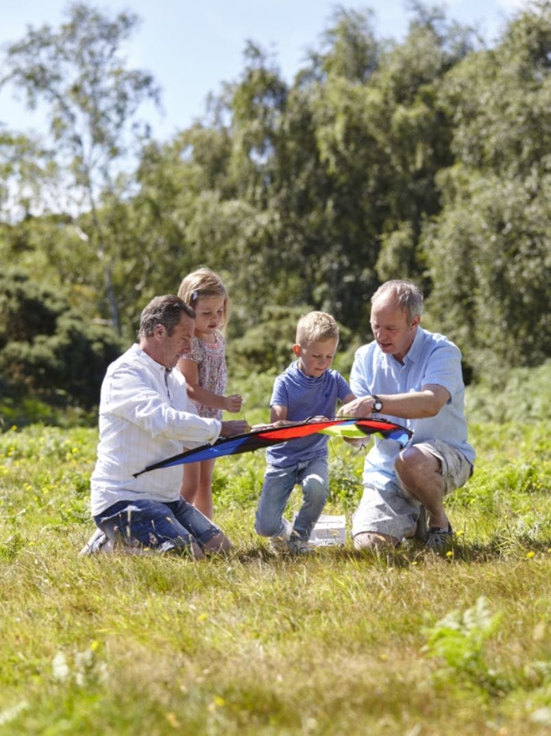 Two dads and two children playing with a kite outside