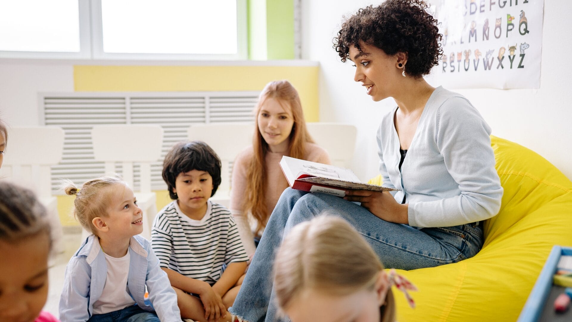Women sat on bean bag reading to children sat around her