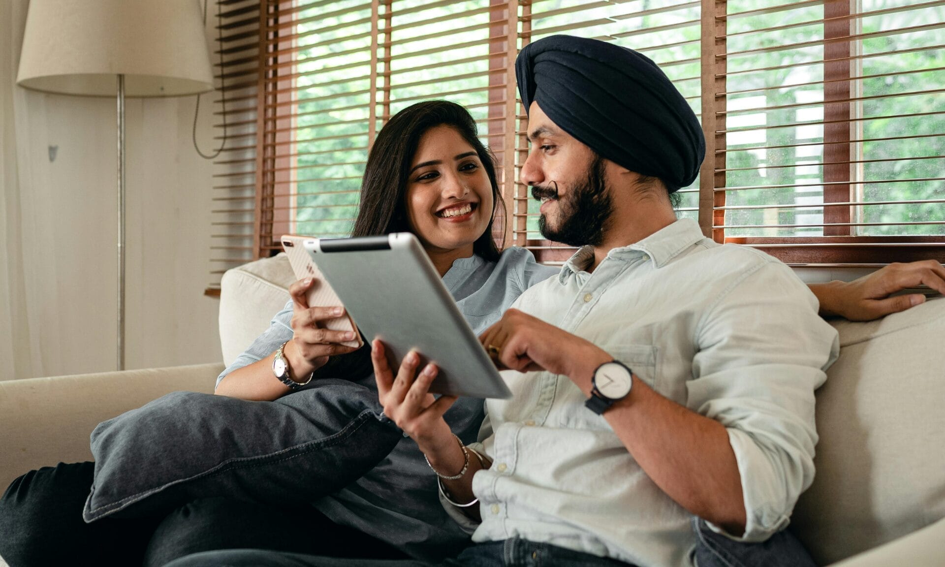 Couple sat on sofa, looking at a phone and tablet